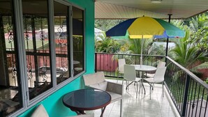 A balcony with a table and chairs, a large umbrella, and a view of a sports field. - MONKEY VIEW: Relaxed Quiet Secure Get Away from the Pto Viejo party + Location!  (Puerto Viejo de Talamanca)