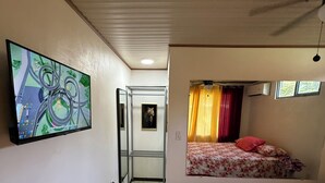 A room with a bed, a television mounted on the wall, and a door leading to another room. - MONKEY VIEW: Relaxed Quiet Secure Get Away from the Pto Viejo party + Location!  (Puerto Viejo de Talamanca)