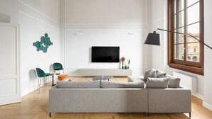 A modern living room with a grey sofa, a flat-screen TV, a coffee table, and a large window. - Apartments Florence - The Wizard's House (Firenze)