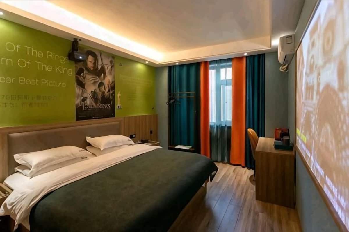 Hotellihuone, jossa on sänky, työpöytä, projektorikangas ja seinä, jossa on elokuvajulisteita.