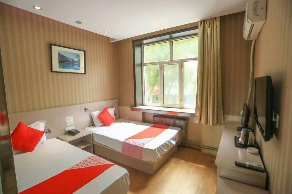 A hotel room with two beds, a window with curtains, a desk with a chair, a TV, and a picture on the wall.