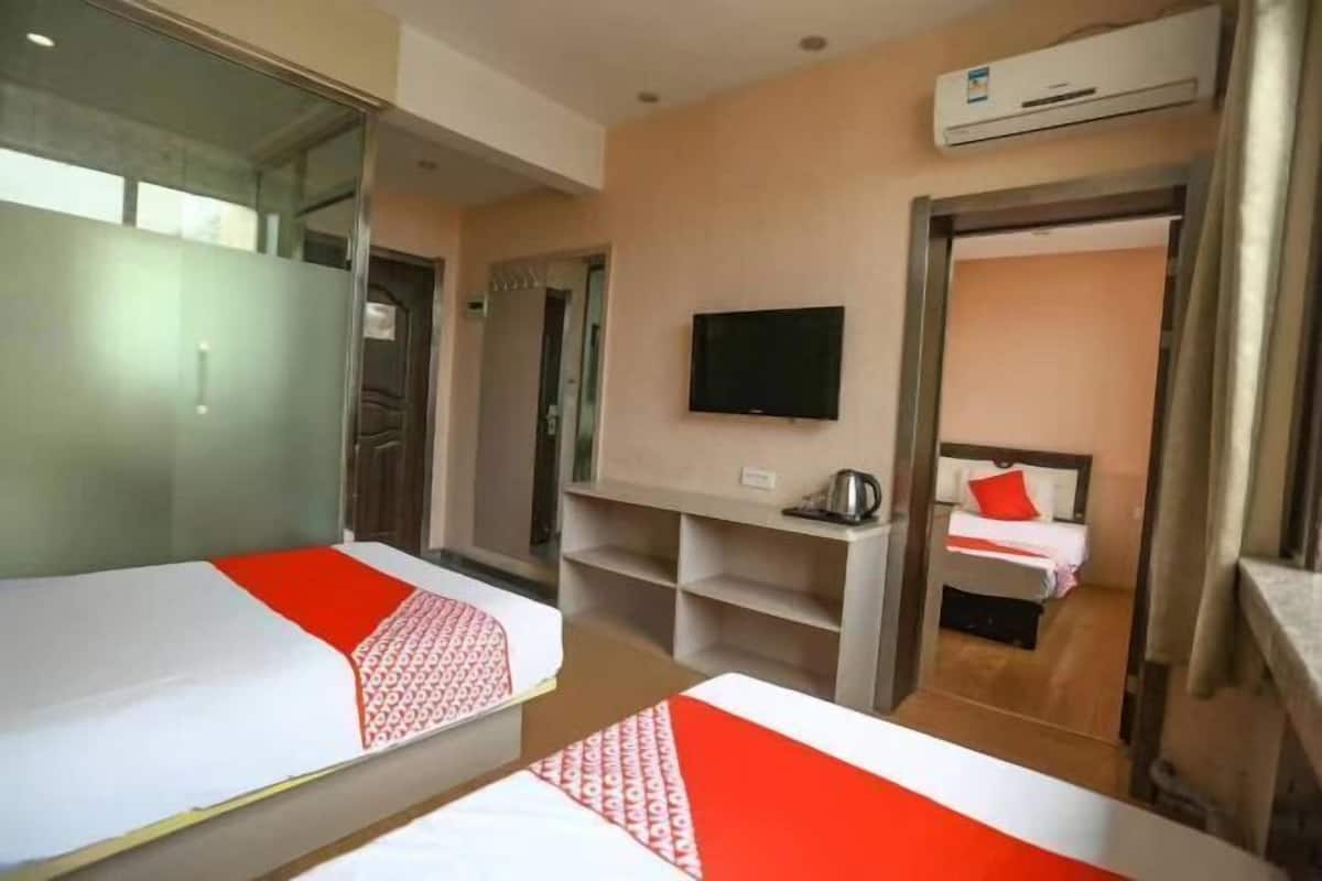 A hotel room with two beds, a TV, a kitchenette, and an air conditioning unit.