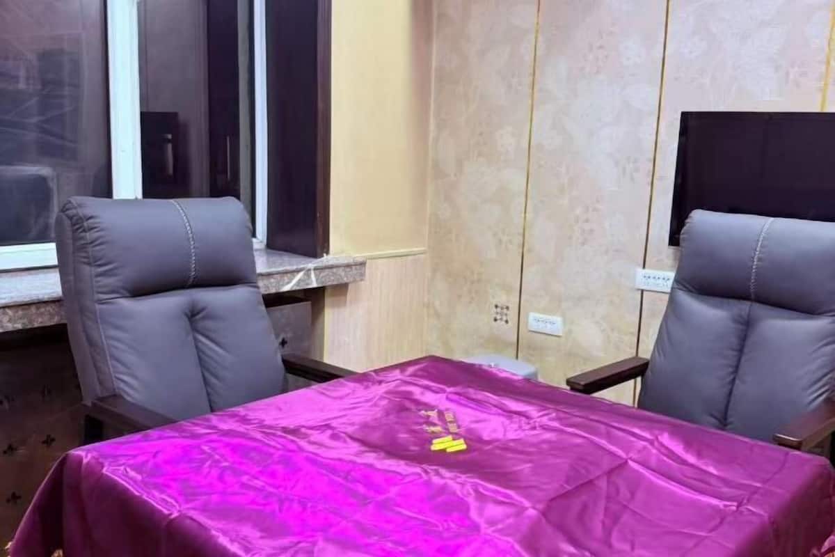 A room with two grey leather chairs, a table covered with a purple cloth, and a window with blinds.