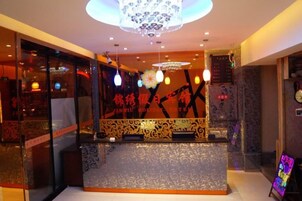 Zona de recepción con una araña, mostrador de recepción y una pared decorativa con caracteres chinos.