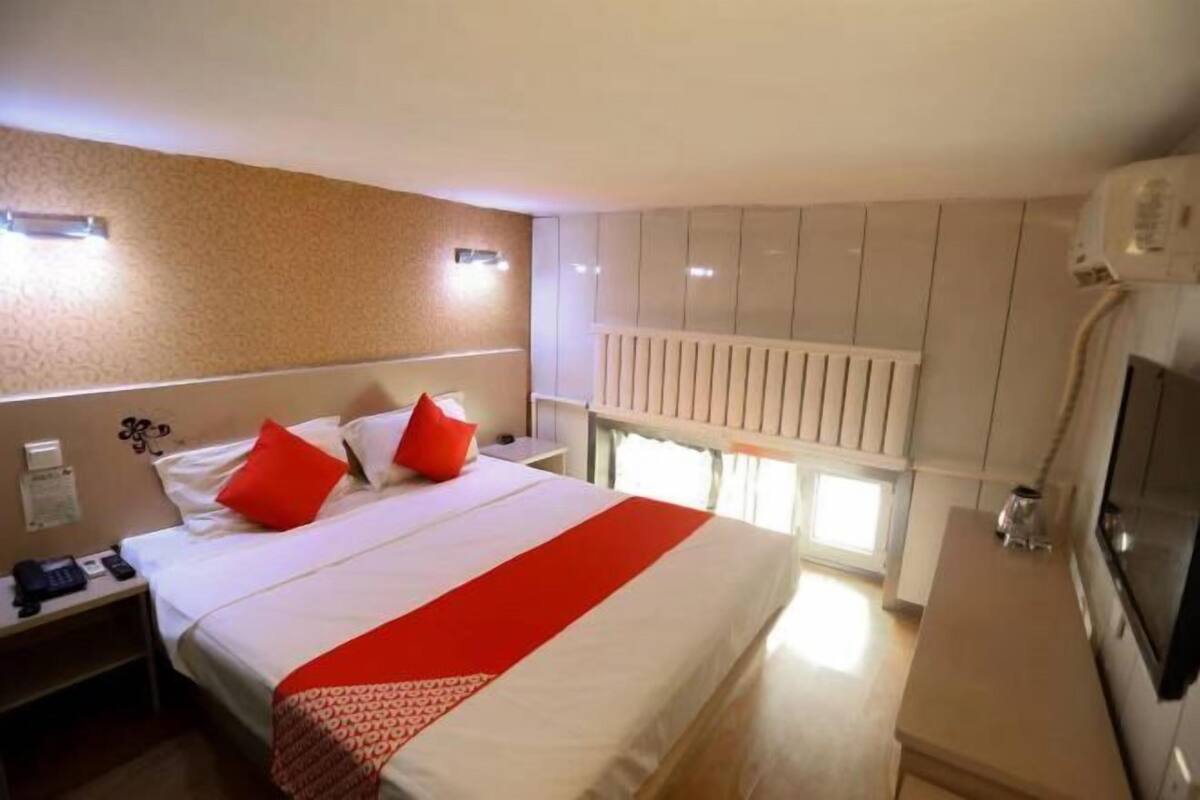 A hotel room with a bed, a nightstand, a desk, a radiator, and a TV.