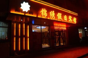 A building with a prominent illuminated sign, large columns, and a visible entrance. - Splendid Holiday Hotel (Mudanjiang)