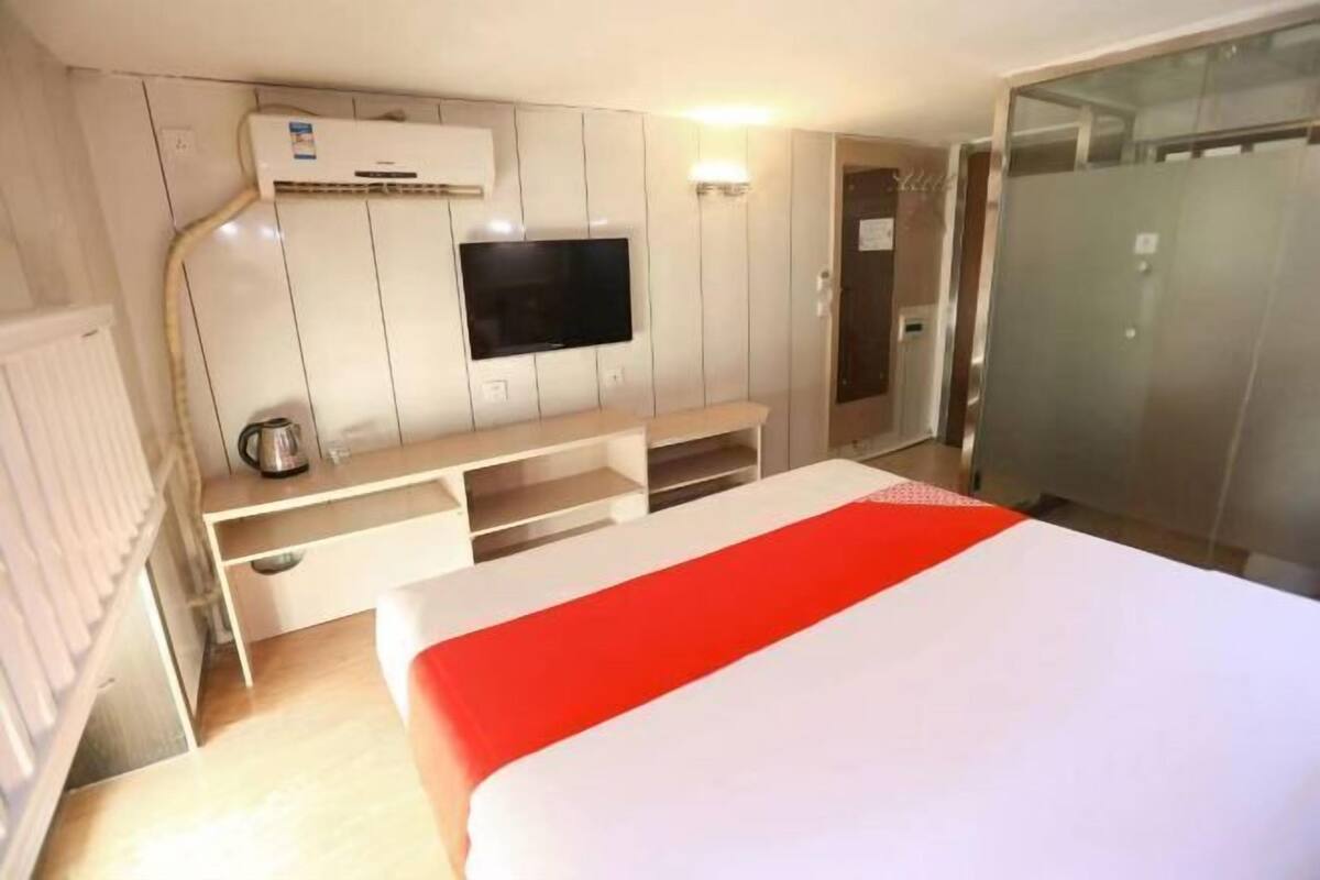 A hotel room with a bed, a TV mounted on the wall, a desk with a kettle, and a wardrobe.