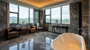 A spacious bathroom with a large bathtub, a seating area with a sofa and chairs, and large windows offering a mountain view. - Zhaofeng International Hotel (Kuancheng)