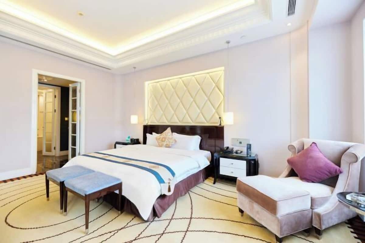 Une chambre d’hôtel avec un grand lit, des tables de chevet, une chaise et un banc.