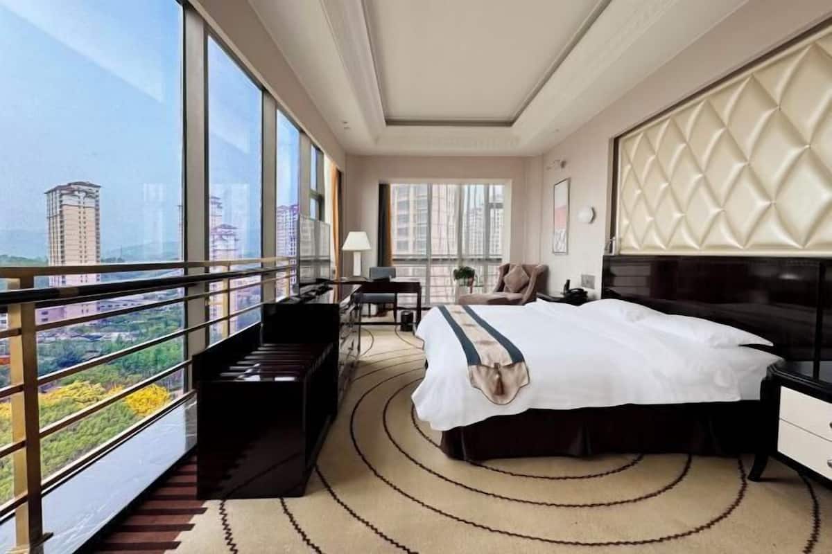 Une chambre d’hôtel avec un grand lit, une télévision, un bureau et une vue sur la ville grâce à de grandes fenêtres.