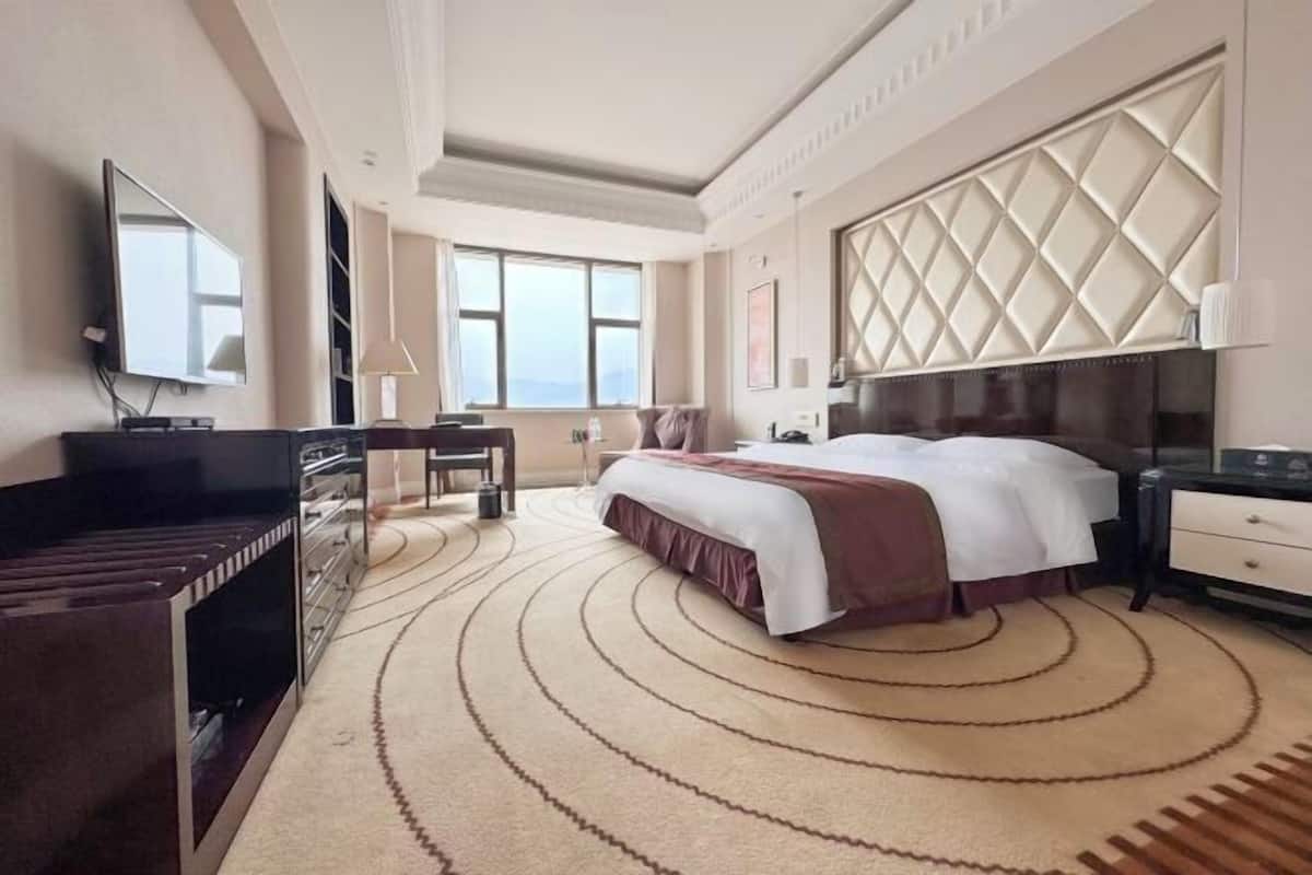 Une chambre d’hôtel avec un grand lit, un bureau avec une chaise, une télévision et une grande fenêtre.