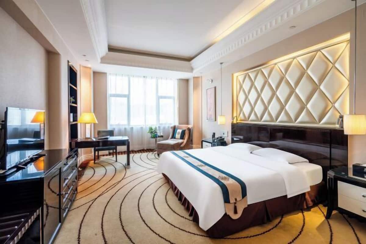 Une chambre d’hôtel avec un grand lit, un bureau, une télévision et un panneau décoratif au mur.