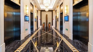 A modern hotel lobby with a marble floor, two elevators, and a central chandelier. - Zhaofeng International Hotel (Kuancheng)