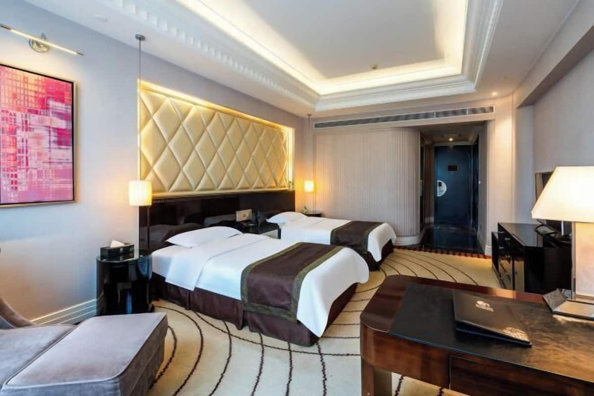 Une chambre d’hôtel avec deux lits, une grande tête de lit rembourrée, un bureau avec un ordinateur portable et un grand tableau accroché au mur.