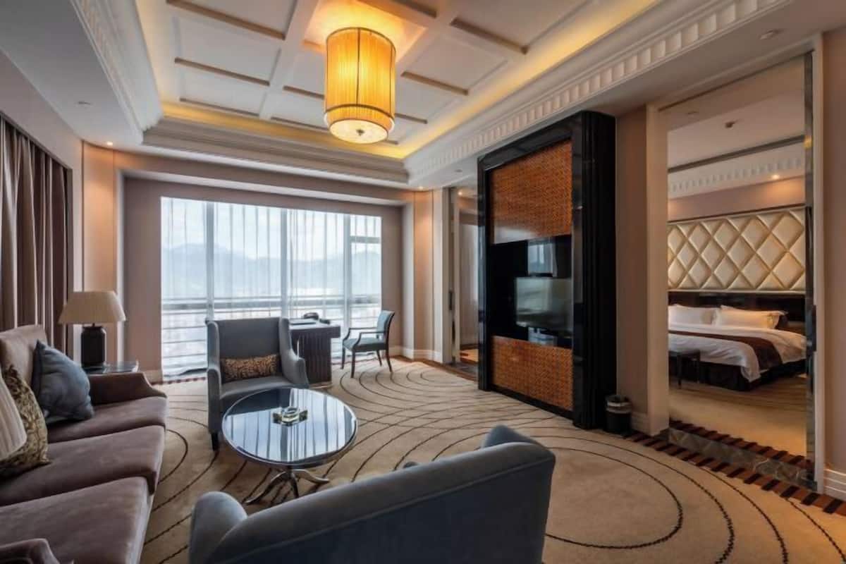 Une chambre d’hôtel moderne avec un canapé, une table basse ronde, un téléviseur et un lit doté d’une tête de lit.
