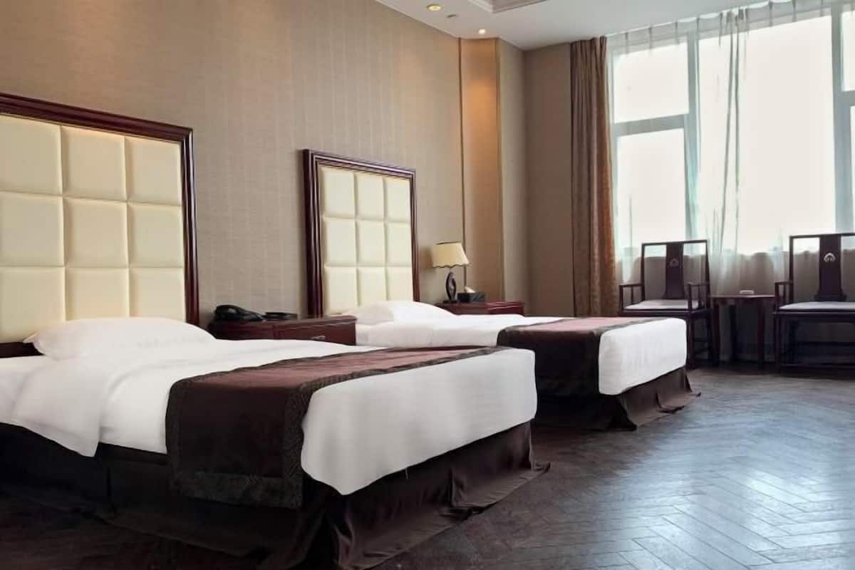 Une chambre d’hôtel avec deux lits, une grande fenêtre avec des rideaux, un bureau avec une chaise et une lampe.