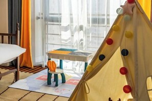 Una habitación con una cama, una mesita con una silla, una carpa de juegos colorida y una ventana con cortinas.