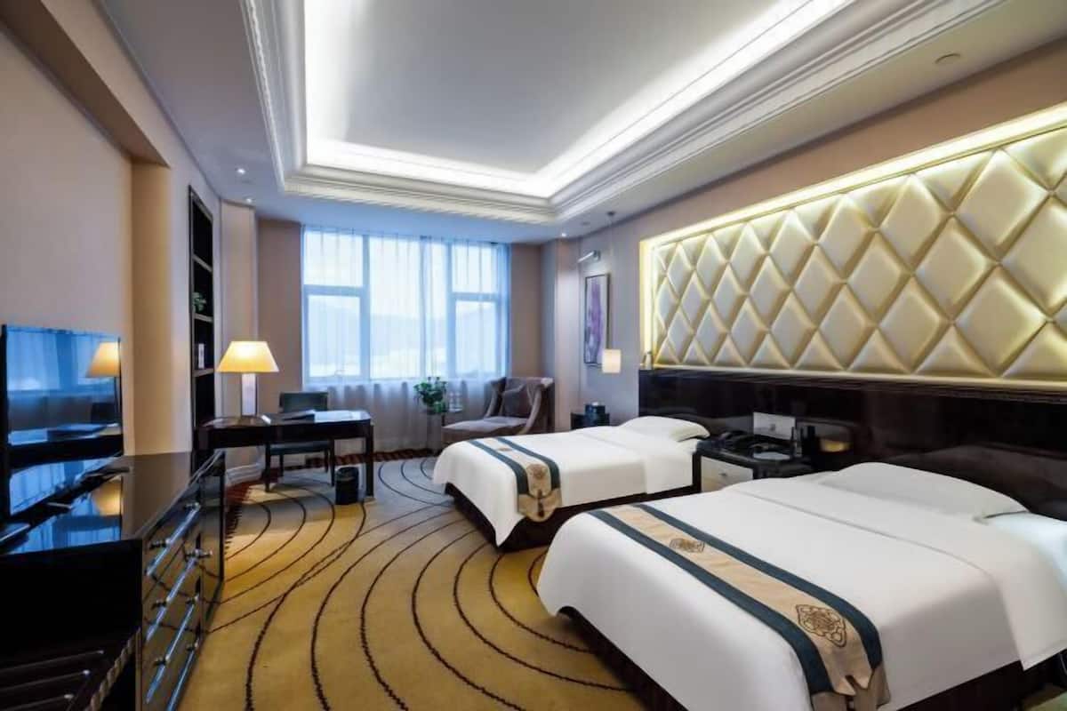 Une chambre d’hôtel avec deux lits, un bureau, une télévision et une grande fenêtre.