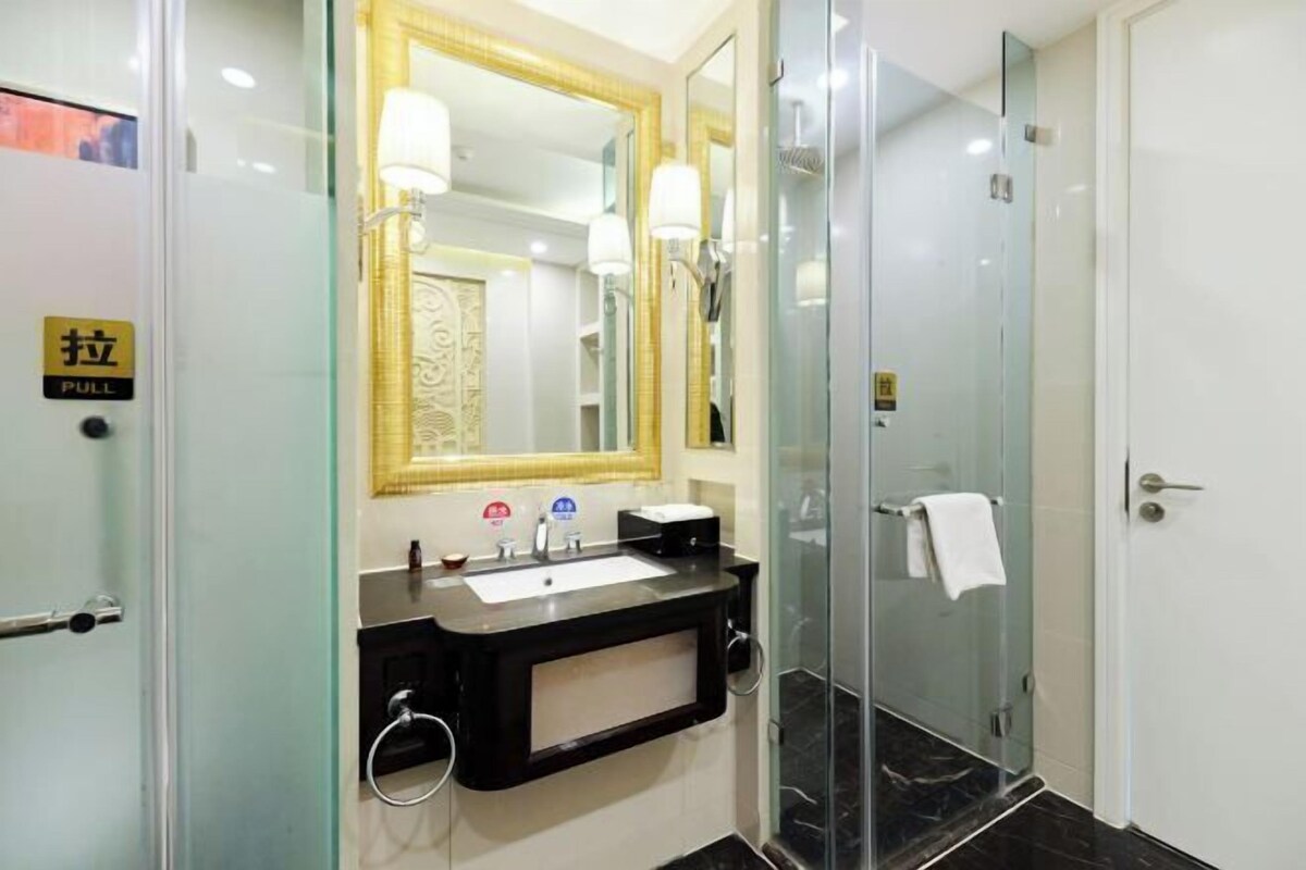 Un baño moderno con cabina de ducha de vidrio, un espejo grande con marco dorado y un lavamanos negro con toallero.