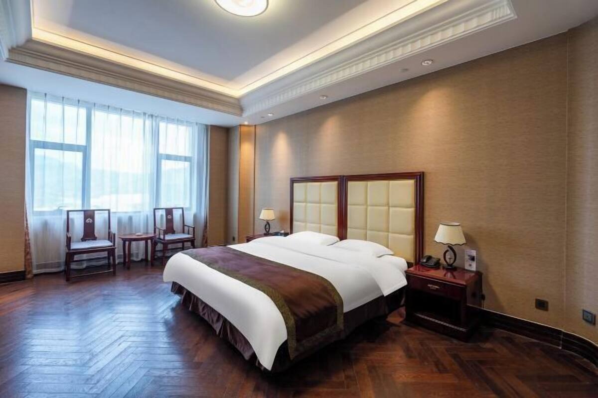 Une chambre d’hôtel avec un grand lit, deux tables de chevet, une chaise et une fenêtre avec des rideaux.