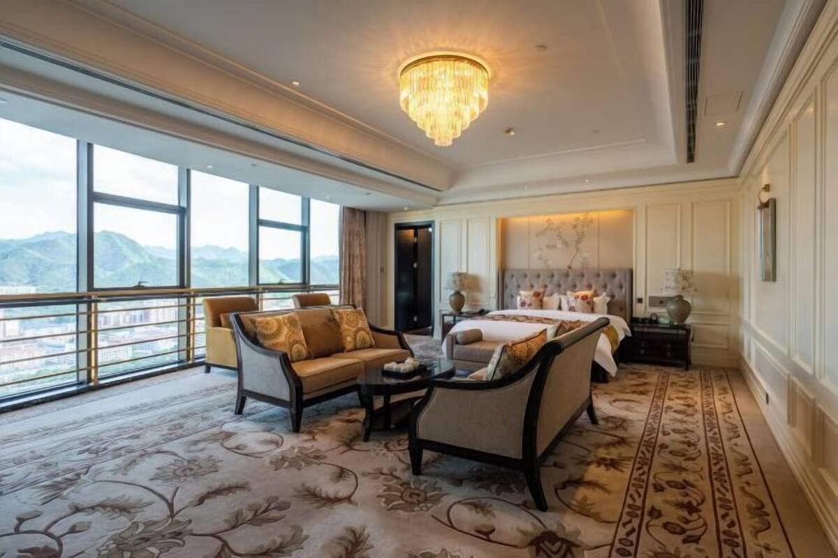 Une chambre d’hôtel spacieuse, dotée d’un grand lit, de deux fauteuils, d’une table basse et offrant une vue sur les montagnes grâce à de grandes fenêtres.