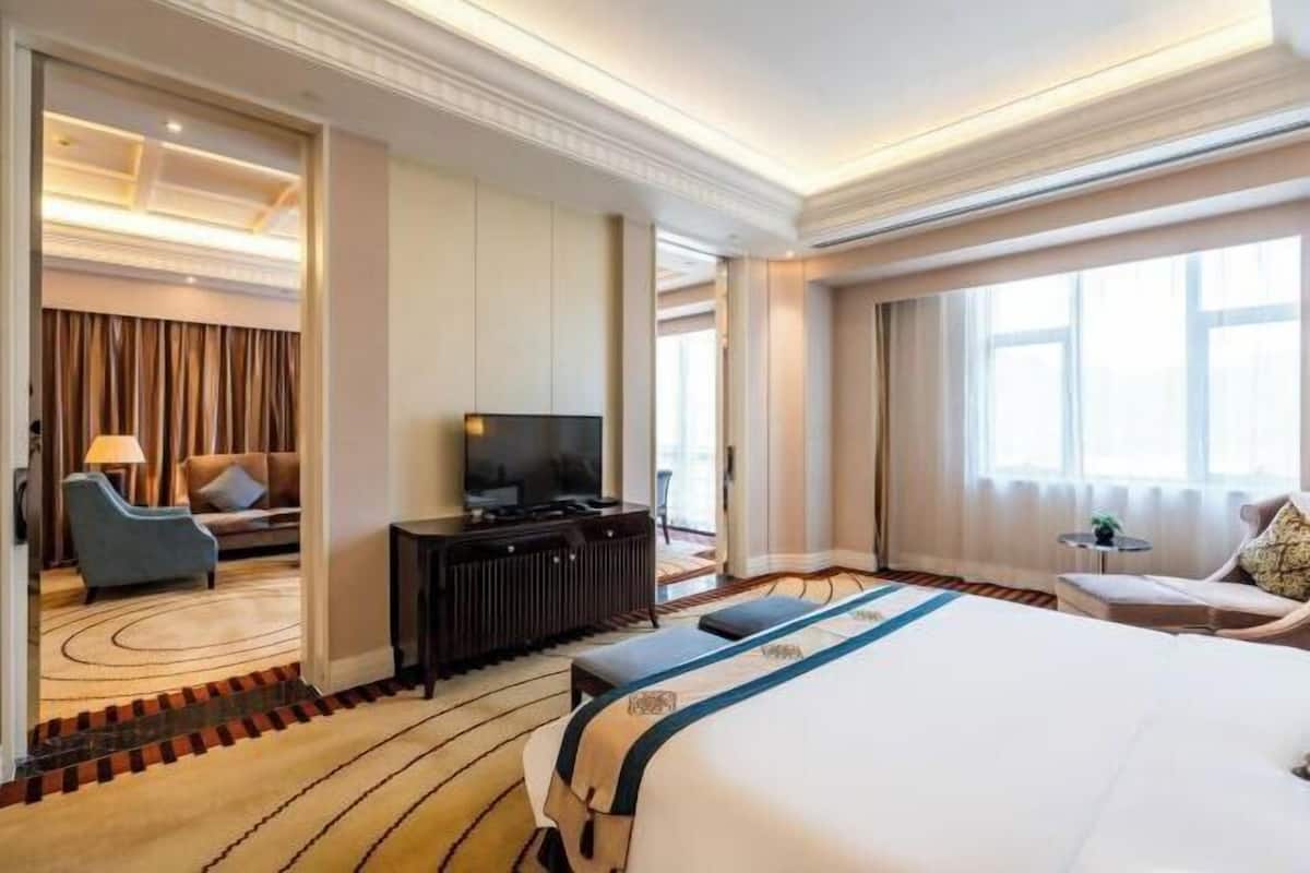 Une chambre d’hôtel dotée d’un grand lit, d’une télévision, d’un coin salon avec un canapé et des fauteuils, et offrant une vue sur l’extérieur.