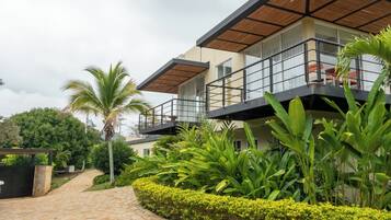 A modern two-story building with a balcony, surrounded by lush greenery and a stone pathway.