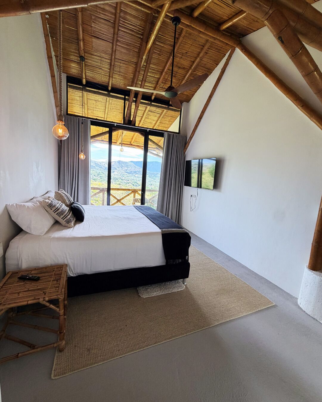Un dormitorio con cama, una mesita, televisor y vistas al exterior.