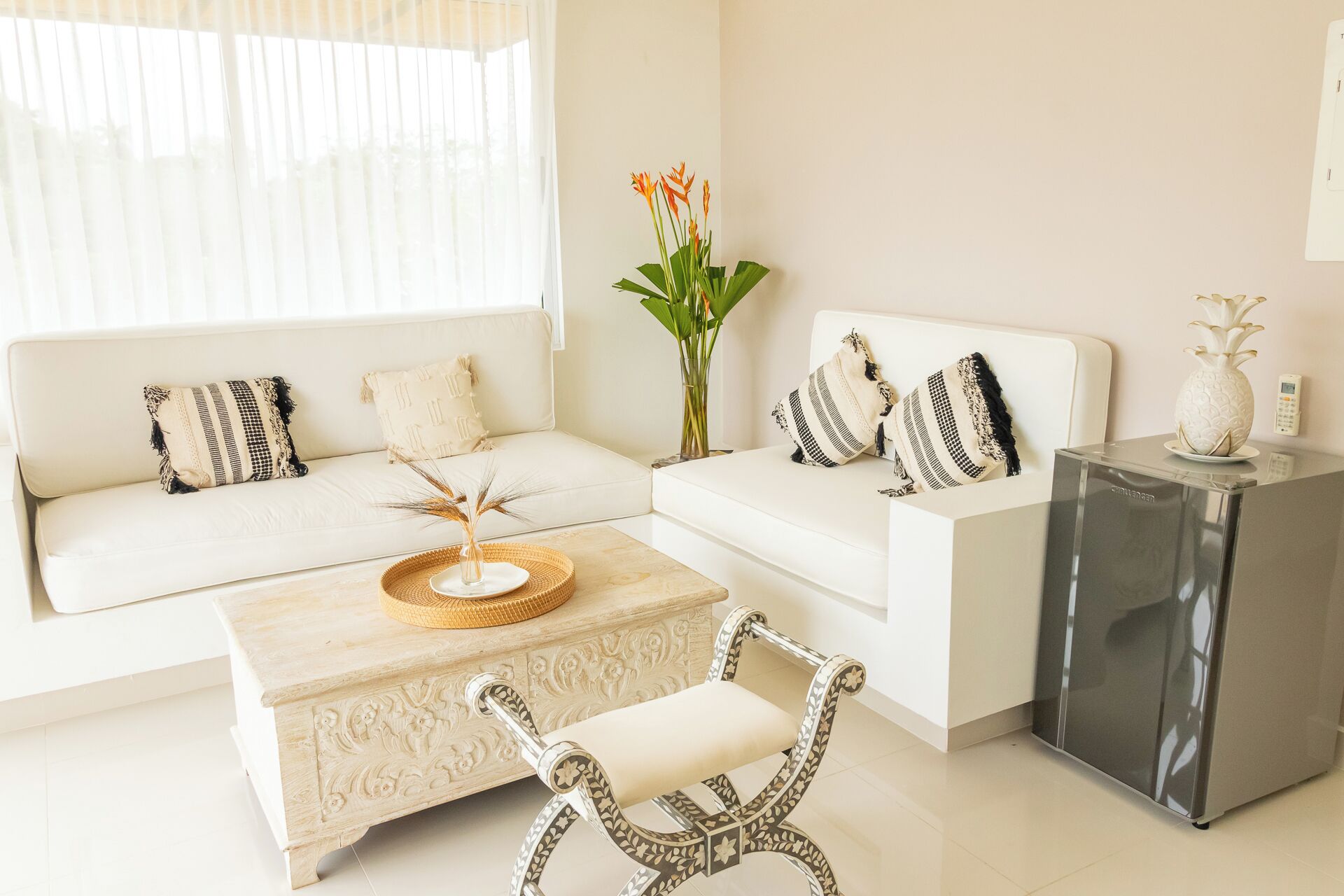 Un salon moderne avec un canapé blanc, une table basse et un fauteuil à motifs. On y trouve une petite table d’appoint sur laquelle est posé un vase de fleurs.