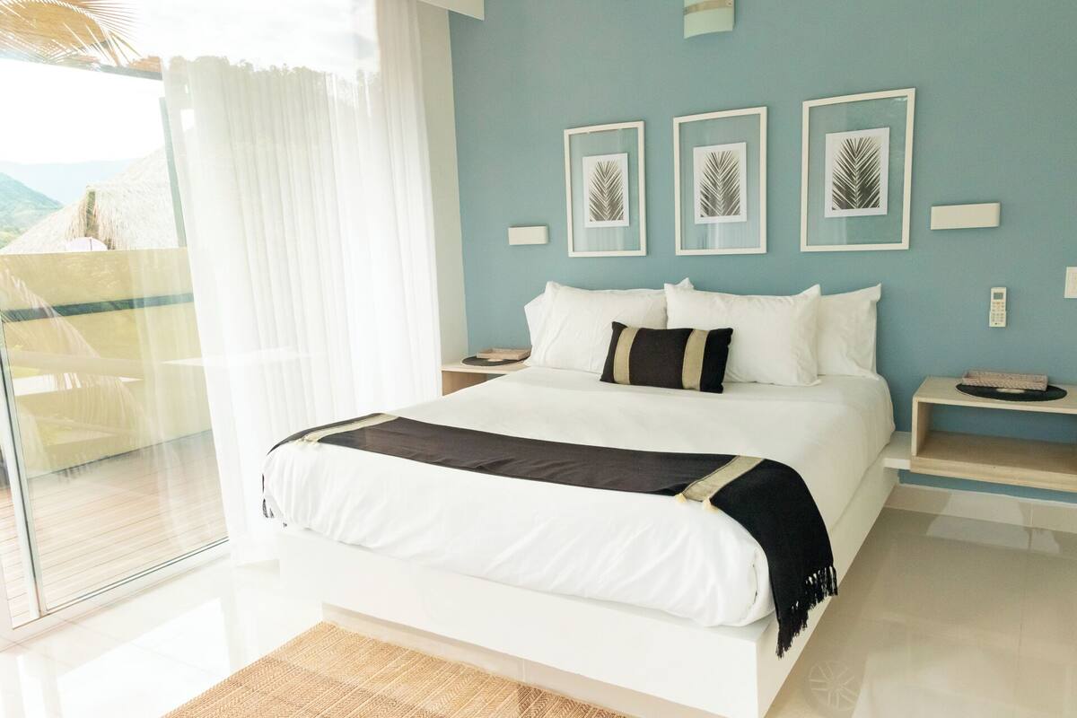 A modern bedroom with a large bed, a glass door leading to a balcony, and framed artwork on the wall.