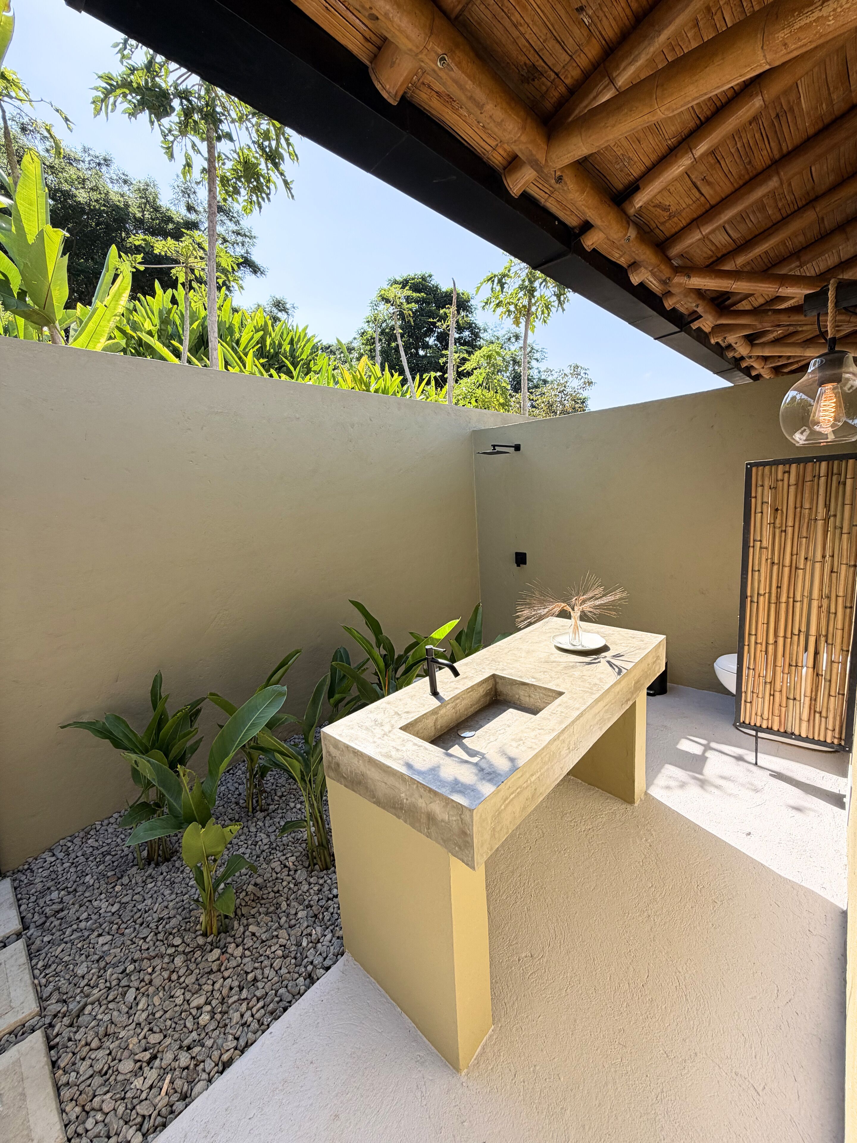 An outdoor kitchen area with a concrete countertop, a black faucet, and a hanging light fixture.