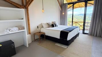 Une chambre à coucher avec un lit, une table de chevet, une étagère avec des serviettes et une vue sur l’extérieur.