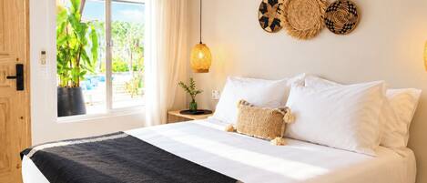 A bedroom with a bed, a window with curtains, a bedside table with a lamp, and wall decor.