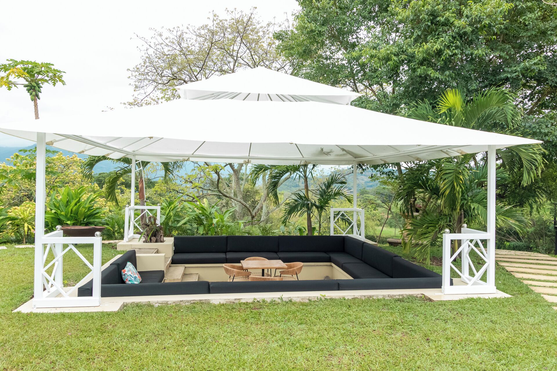 A covered outdoor seating area with a white canopy, black cushions, and wooden furniture.