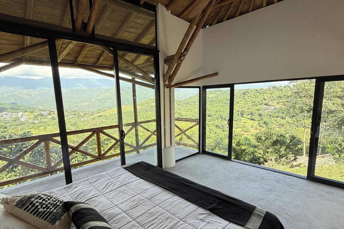 A spacious room with a large bed, wooden ceiling beams, and a view of lush green hills.