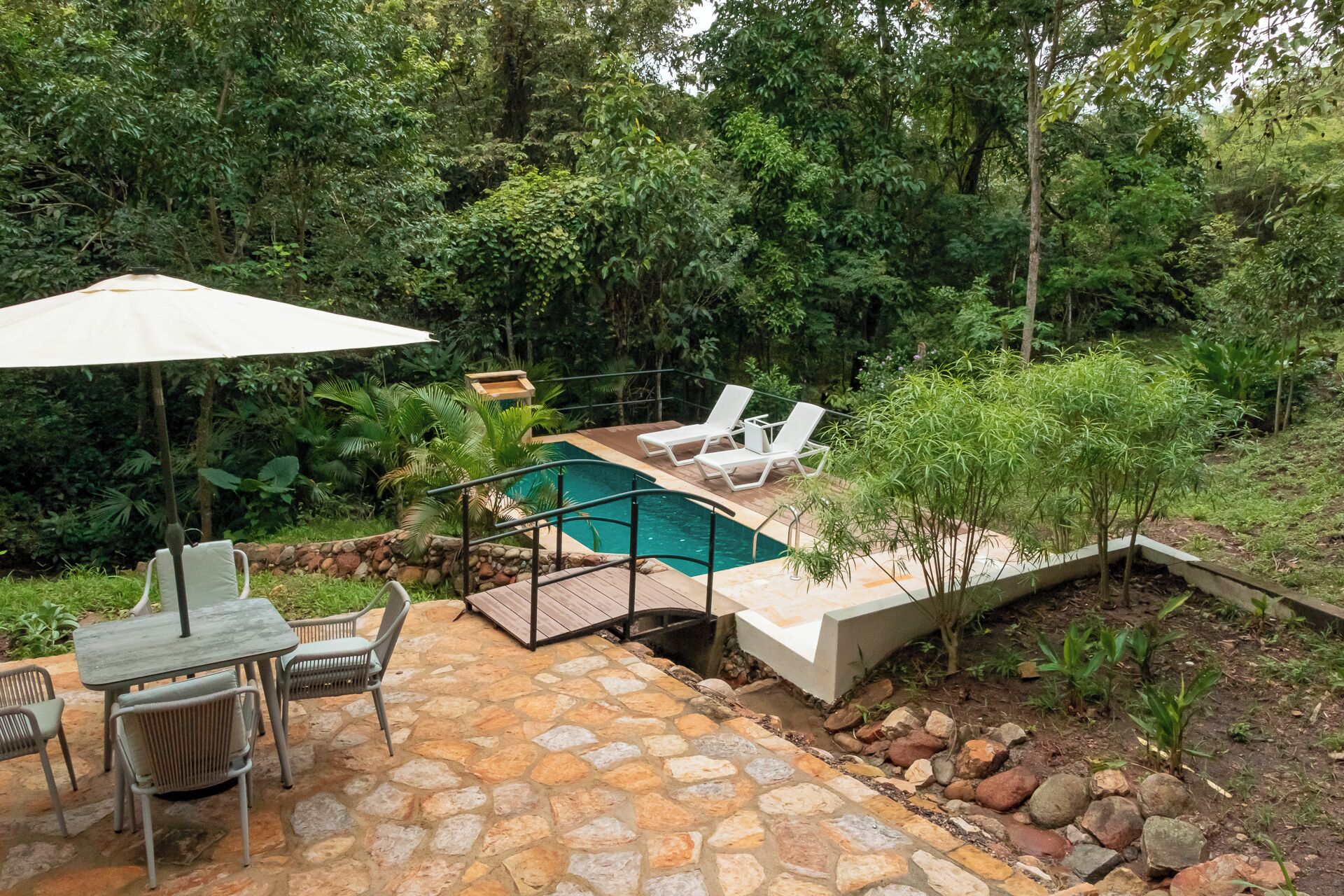 Un patio de piedra con piscina, sillas de descanso y una mesa con sillas.