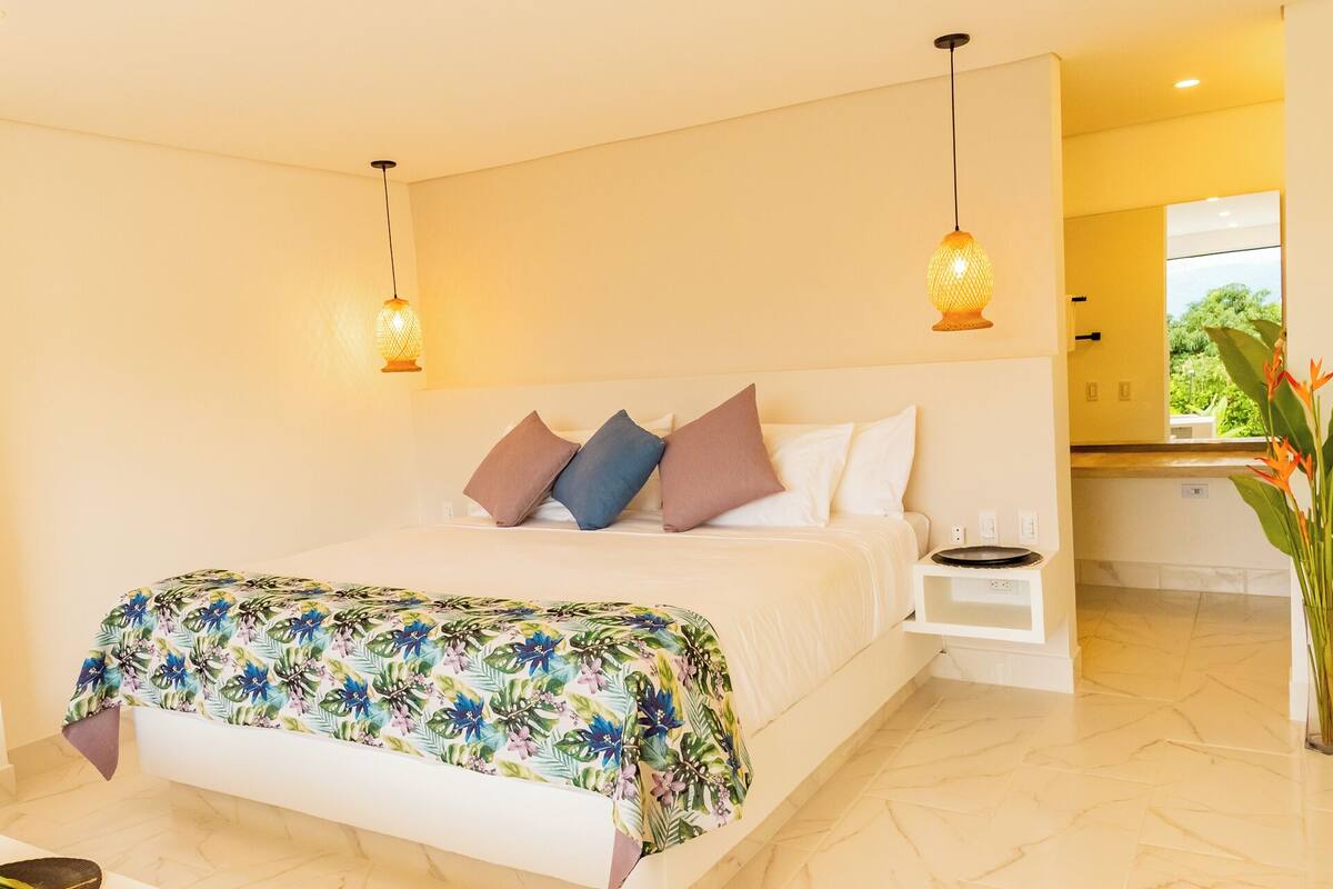 A hotel room with a bed, a nightstand, and a view of the outside.