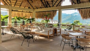 Un espacio de estar al aire libre cubierto, con muebles de mimbre, un sofá y plantas en macetas.