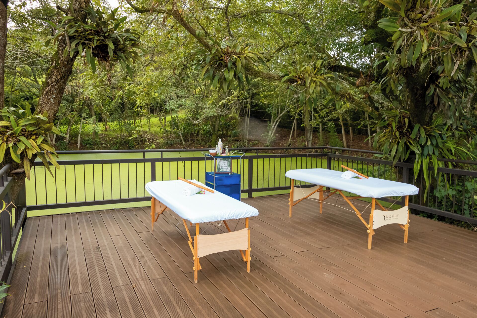 Una terraza de madera con dos camillas de masaje, un bote de basura azul y un letrero que dice 'Master Massage'.