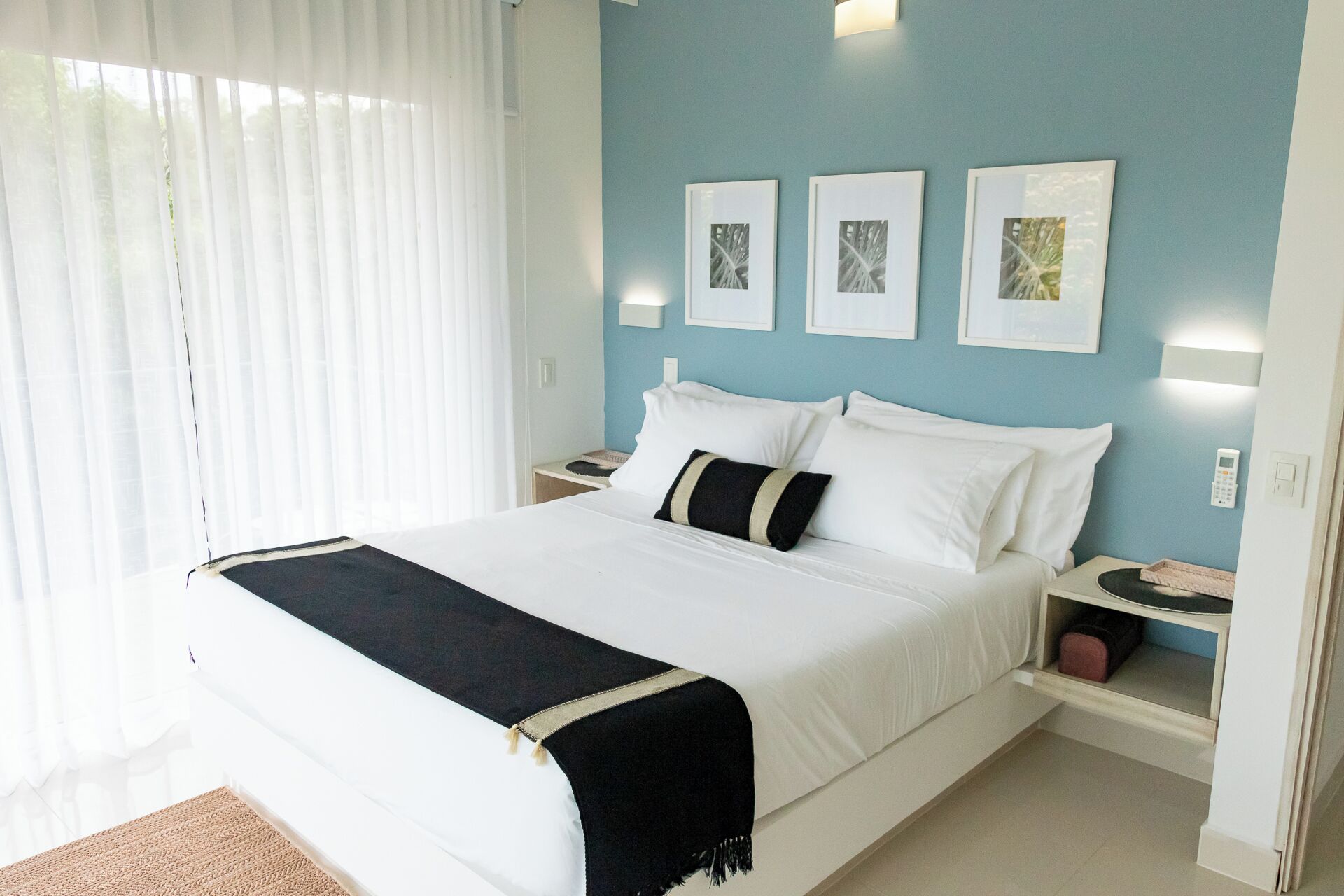 Una habitación de hotel con una cama grande, ropa de cama blanca, una manta negra y tres cuadros en la pared.