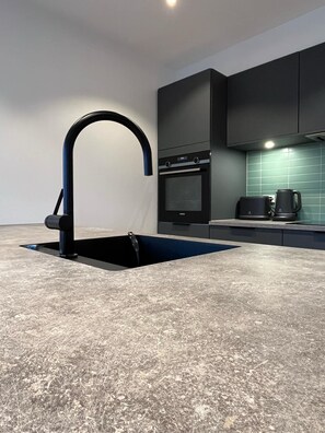 A modern kitchen with a unique sink design, a built-in oven, and a coffee maker. - ATCON Downtown Apartments (Nuuk)