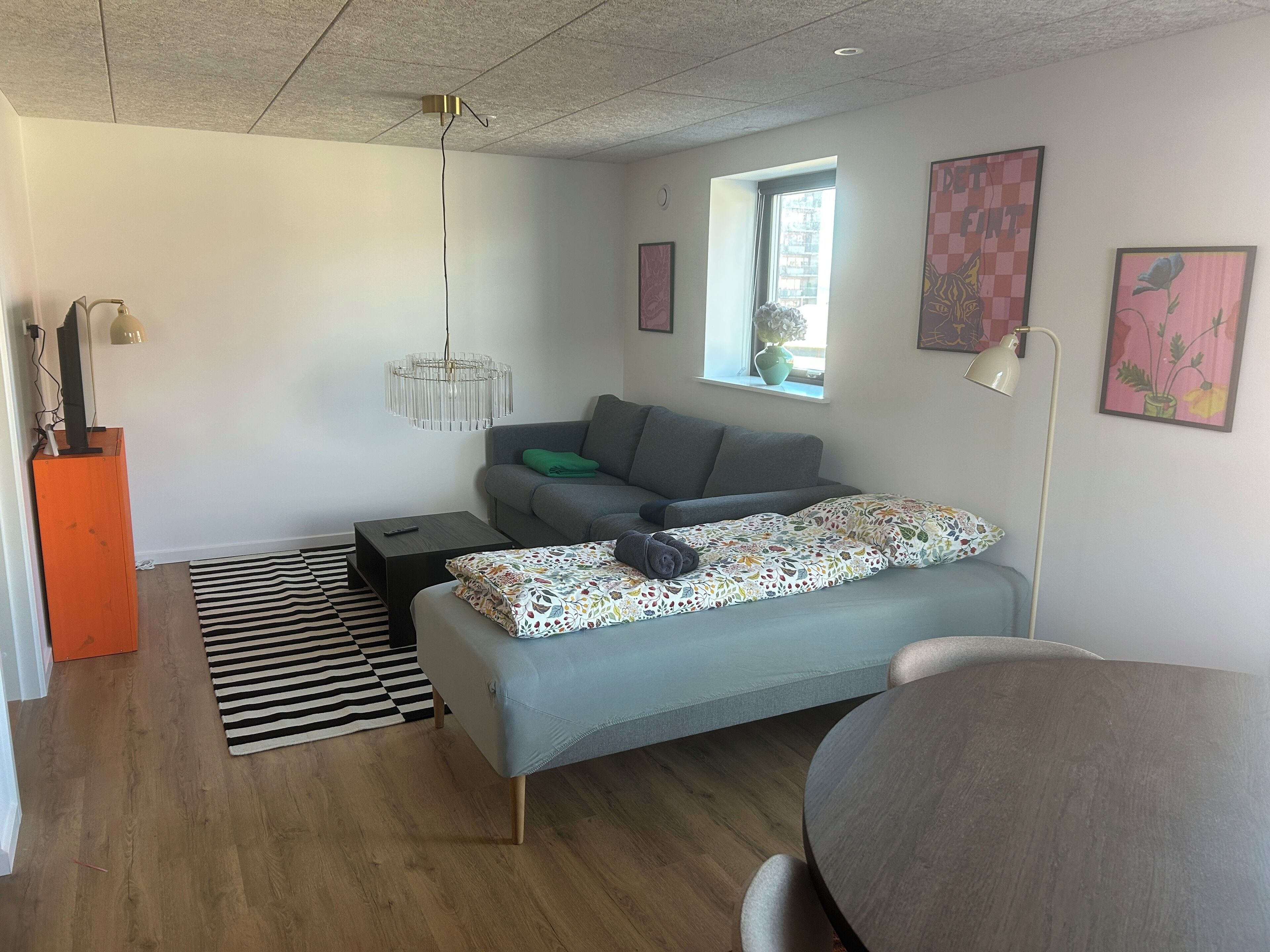 A modern living room with a sofa, a coffee table, a lamp, a TV on a stand, and a window with a view.