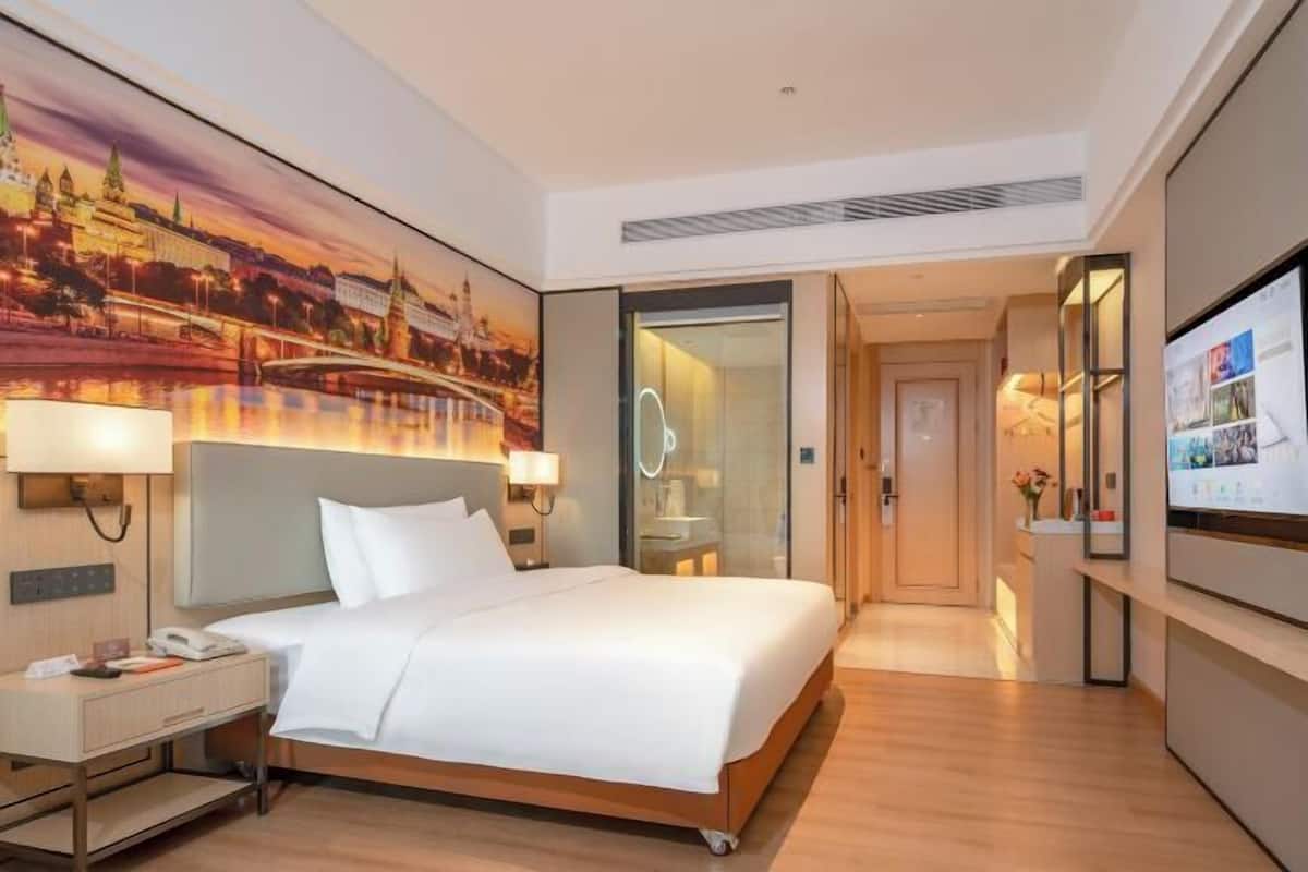 A hotel room with a bed, bedside tables, a TV, and a painting of a cityscape.