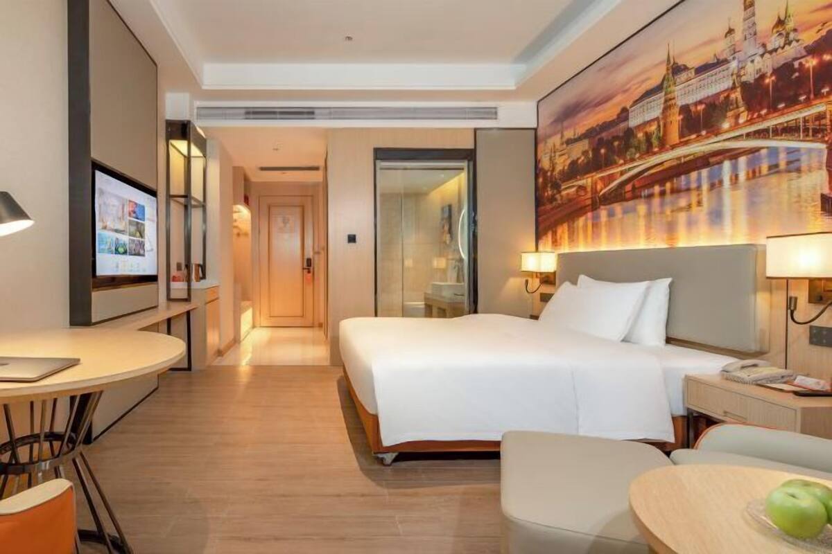 A hotel room with a bed, bedside table, lamp, and a TV on a stand.