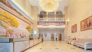 Un hall d’entrée spacieux avec un plafond haut, un magnifique lustre, un comptoir de réception et un balcon aménagé avec des sièges.