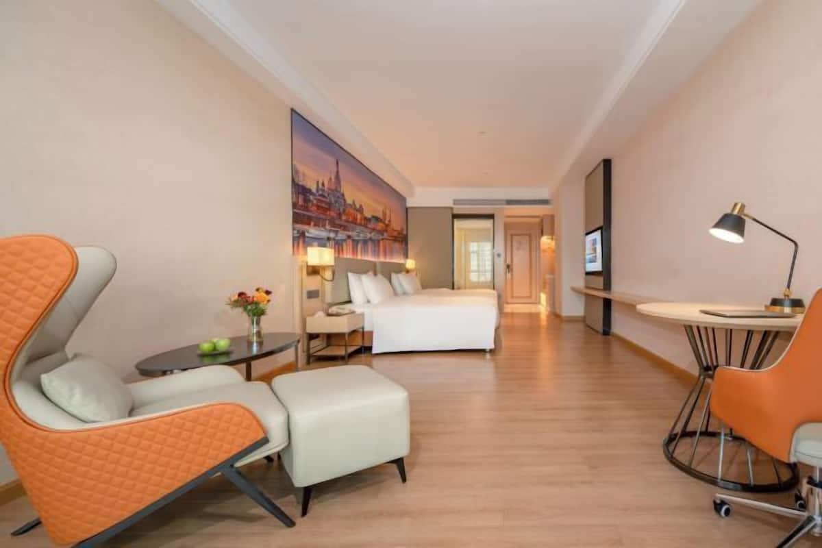 A hotel room with a bed, a desk, a chair, and a sofa.