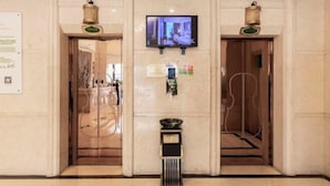 Un hall d’entrée avec un téléviseur fixé au mur, une poubelle et deux portes ornées d’éléments décoratifs.