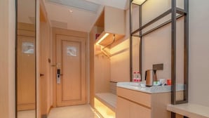 Une chambre d’hôtel moderne avec une porte en bois, un petit coin salon, une coiffeuse avec un miroir et un plan de travail avec des articles de toilette.