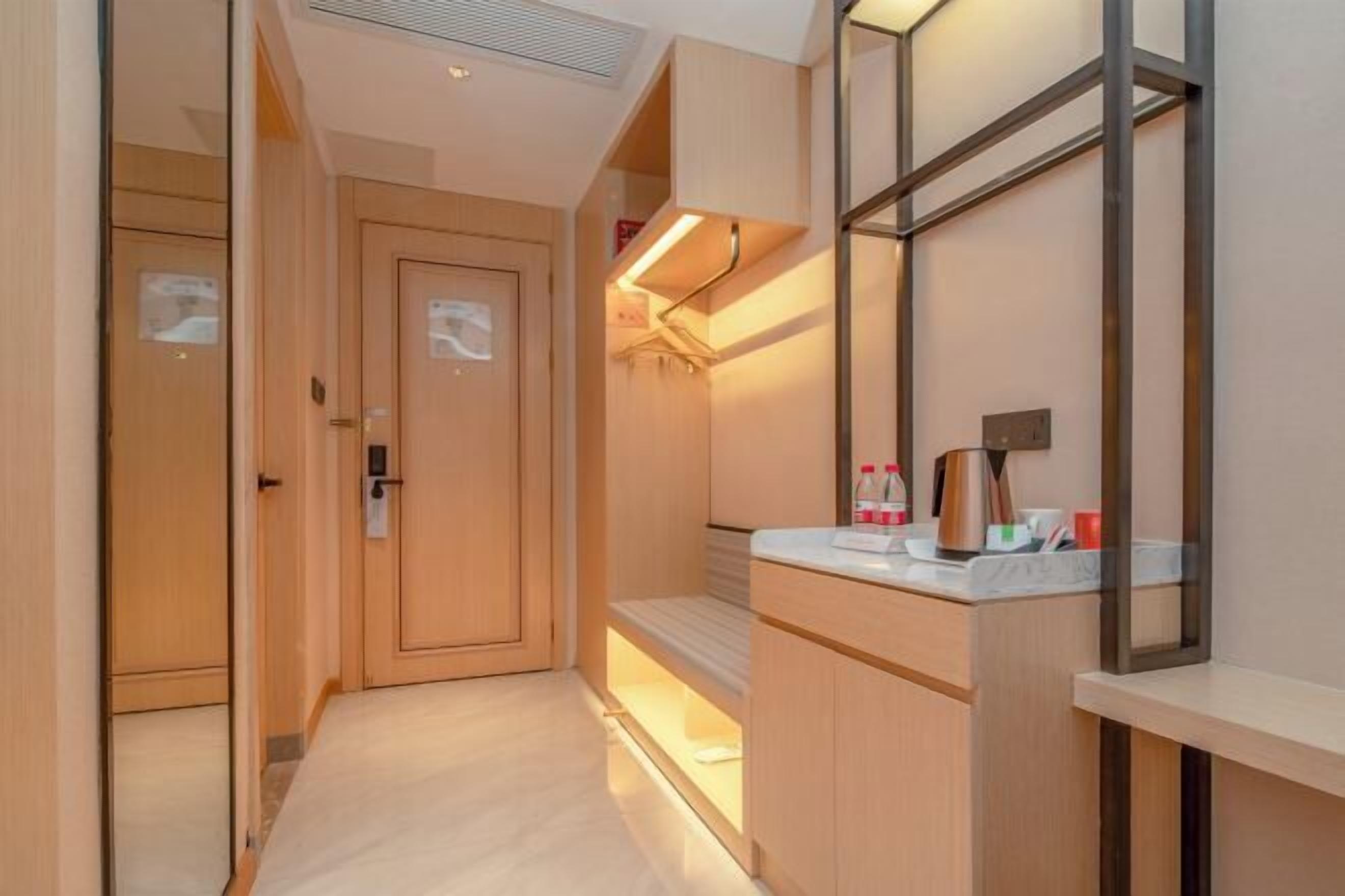 A hotel room with a wooden door, a bedside table with a mirror, and a small seating area.