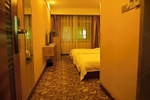 Habitación de hotel con alfombra estampada, cama, mesita de noche, espejo y ventana con cortinas.